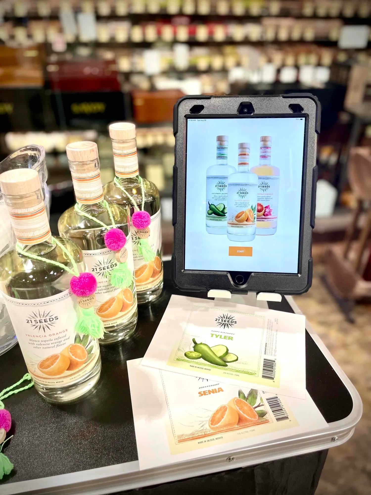 A 21Seeds personalisation stand: bottles with tassels, the app on an iPad and printed labels for Tyler and Senia