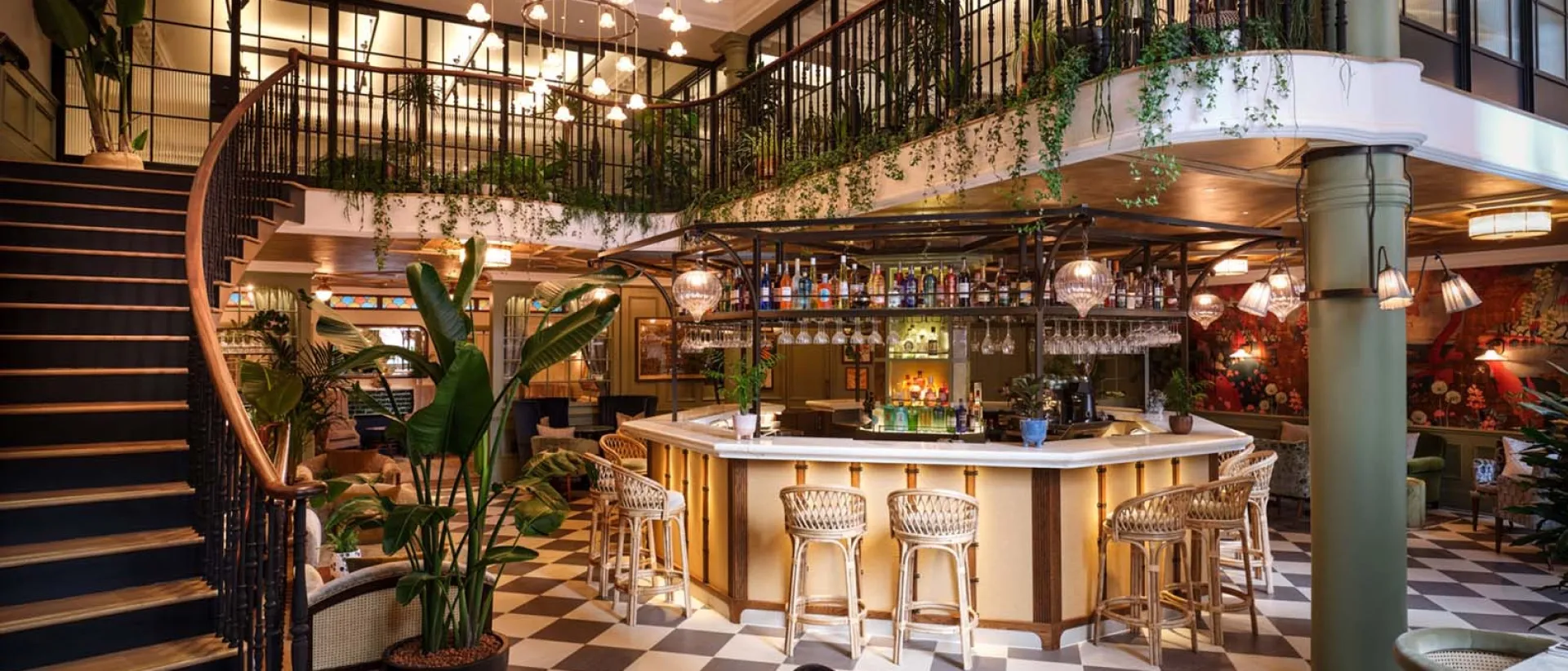 The bar at a Pavilion clubhouse, with a curving staircase, hanging plants and a chequered floor